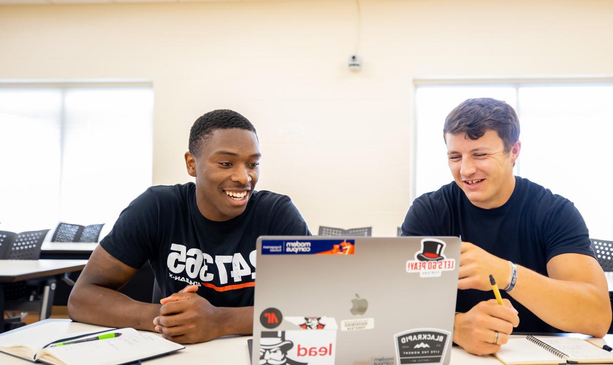 Two students in the classroom discussing something on the laptop.